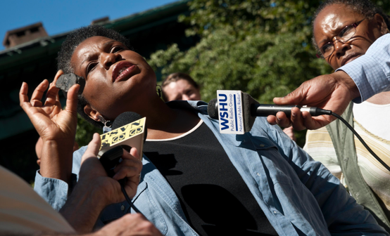 A woman speaks to journalists, holding a microphone in front of her.