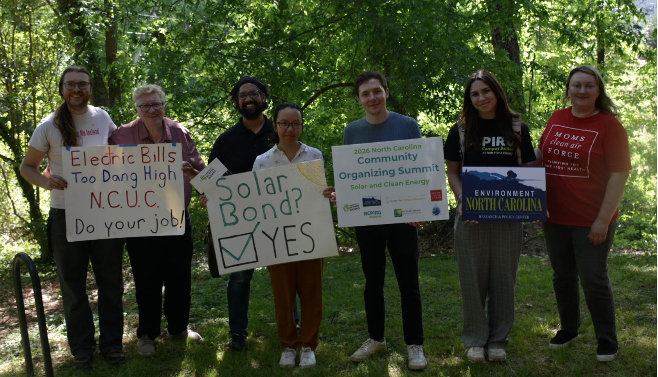 Seven people outdoors holding signs about solar energy and environmental advocacy, in a park setting.